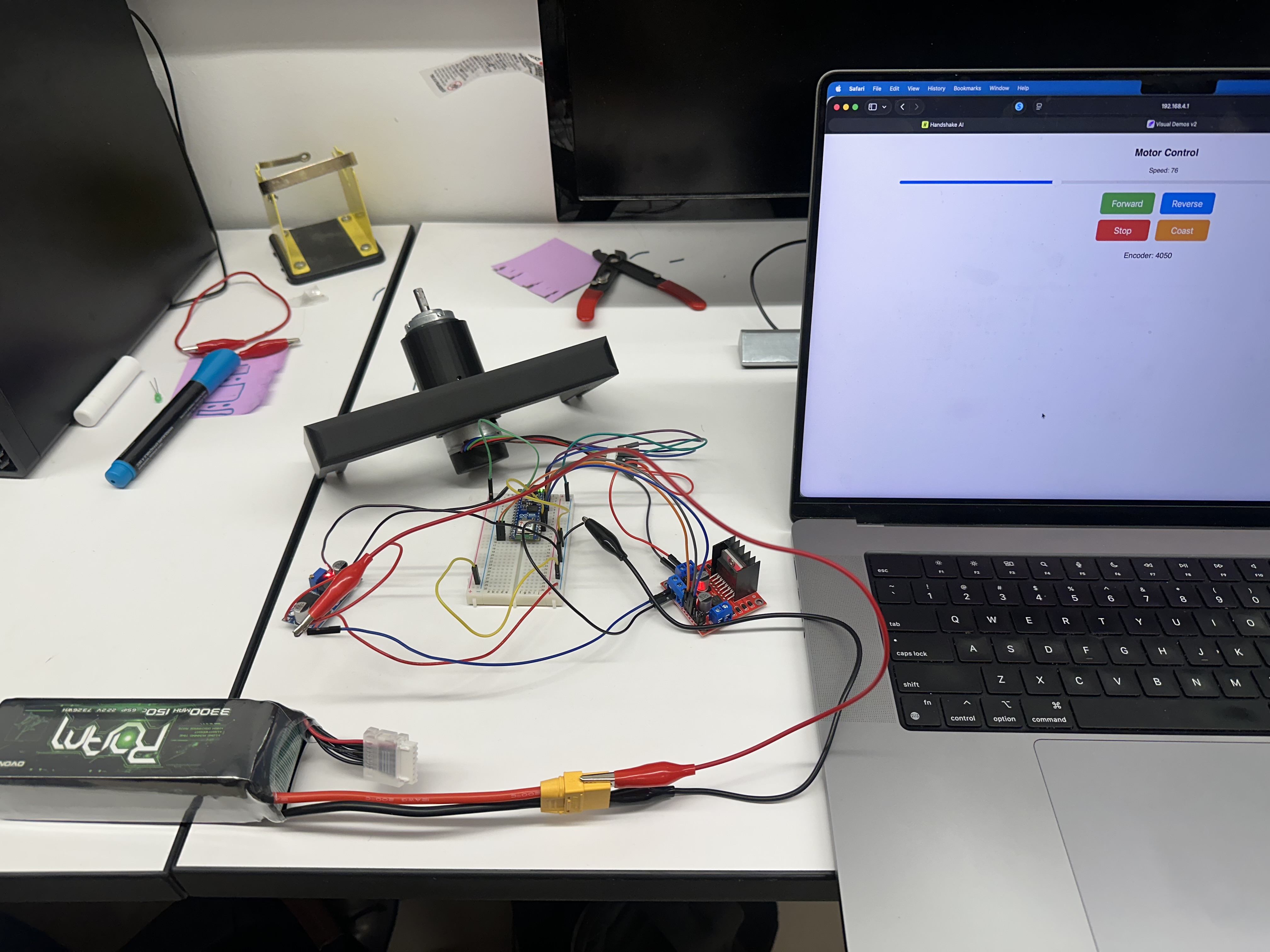 Bench setup driving the motor over WiFi: ESP32, L298N driver, LM2596 buck, and 6S LiPo connected to the geared motor with the WiFi motor-control web UI open on a laptop.