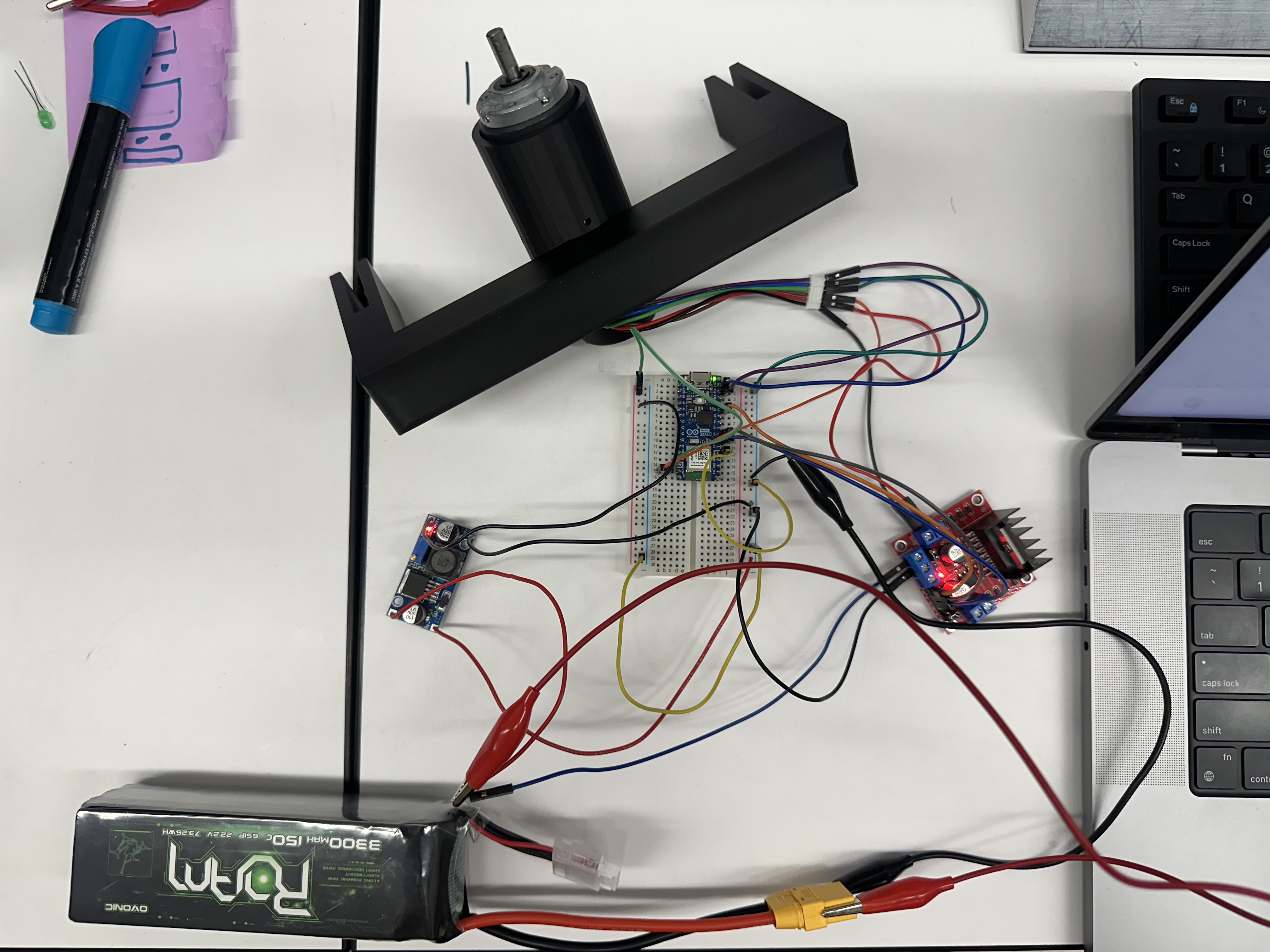 Top-down view of the bench electronics: motor on a 3D-printed mount, breadboard with ESP32, LM2596 buck converter, L298N driver, and a 6S LiPo battery.